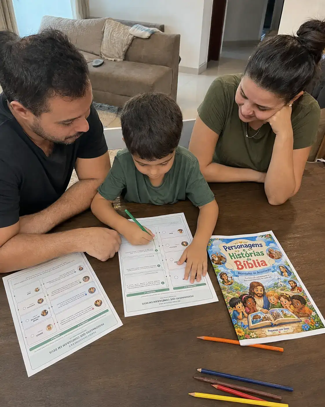 Pai, mãe e filho reunidos à mesa realizando atividades bíblicas impressas